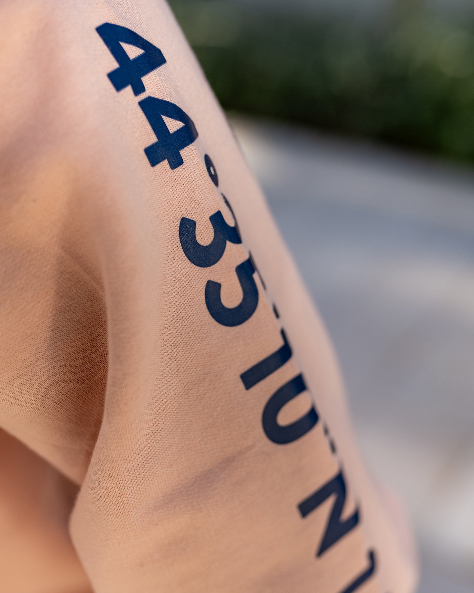 A girl wearing a peach hoodie with navy blue screen printed Lošinj island coordinates on the sleeve and the words Lošinj island on the hood, standing outdoors.