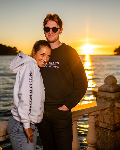 A girl wearing a blue hoodie with white screen printed Lošinj island coordinates on the sleeve and the words Lošinj island on the hood, standing outdoors. Original design by Bongolala.