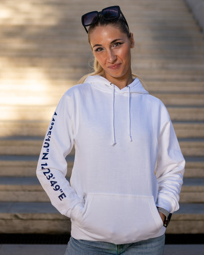 A girl wearing a white hoodie with navy blue screen printed Lošinj island coordinates on the sleeve and the words Lošinj island on the hood, standing outdoors.