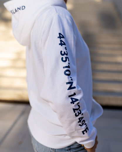 A girl wearing a blue hoodie with white screen printed Lošinj island coordinates on the sleeve and the words Lošinj island on the hood, standing outdoors. Original design by Bongolala.