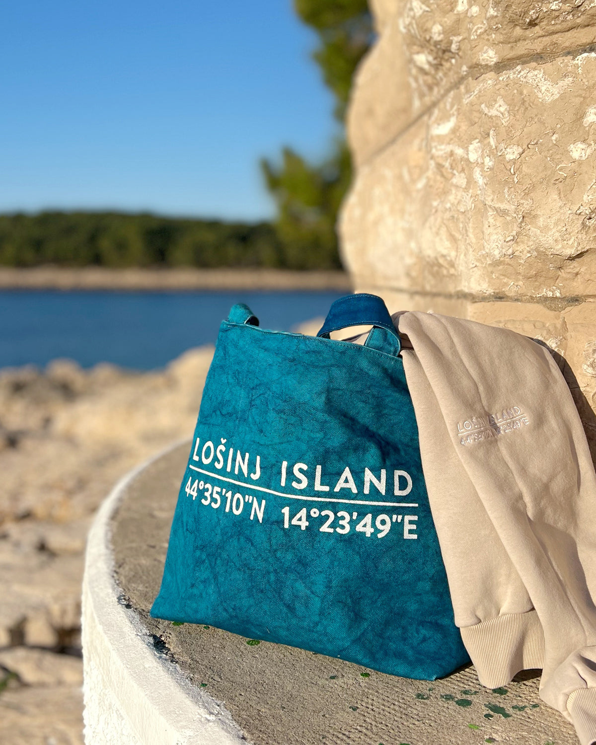 Oversized cotton canvas shopper bag in teal with white screen printed Lošinj Island coordinates design on one side.