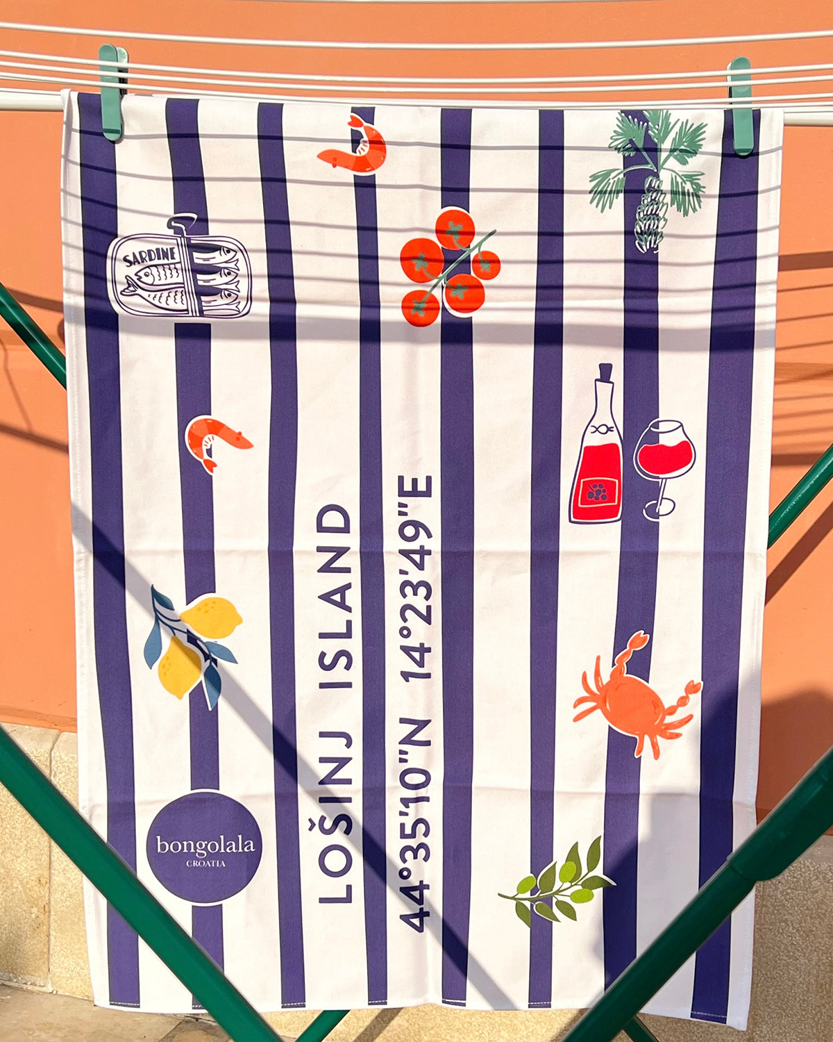 Cotton tea towel with blue nautical stripes and Lošinj Island coordinates design hanging on a clothes line.