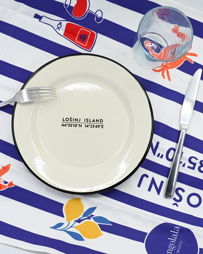 Cream enamel plate with Losinj coordinates design with a black rim on a blue and white striped tea towel with artistic designs and Losinj island coordinates.