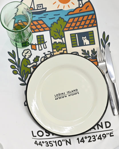 Dinner setting with a cream enamel plate with Losinj coordinates, cutlery, and placemat featuring a scenic illustration of Losinj Island.